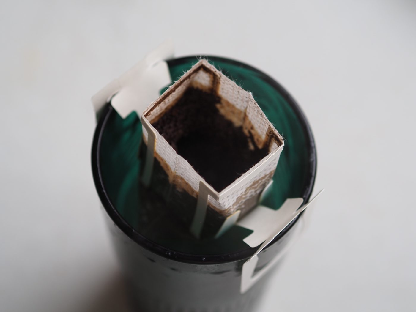 Water poured into a drip coffee bag, with dark coffee below in the cup