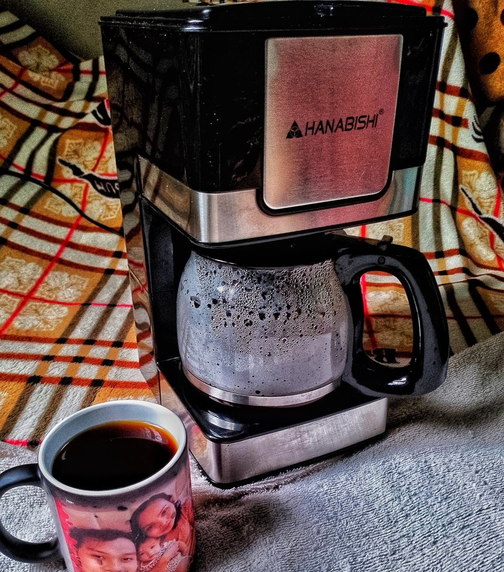A drip filter coffee machine with a glass carafe of brewed coffee and a full mug beside it