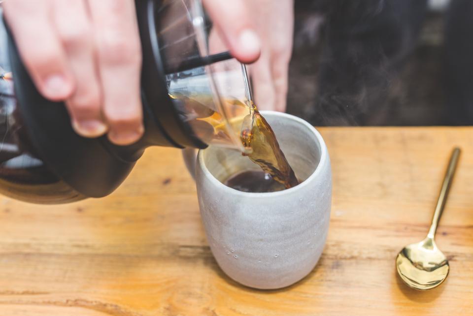 Brewed coffee being poured from a glass carafe into a ceramic mug