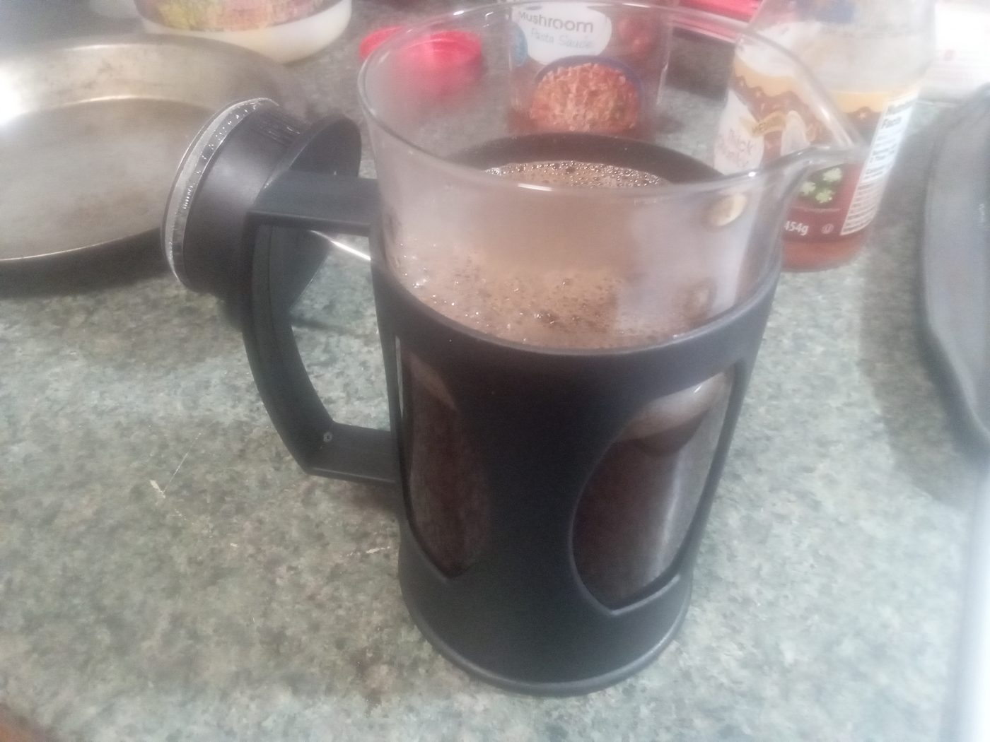 A glass cafetière full of brewed coffee with the plunger raised